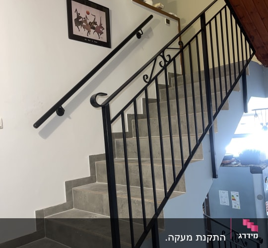 גרם מדרגות עם מעקה מתכת ותמונה ממוסגרת על הקיר
